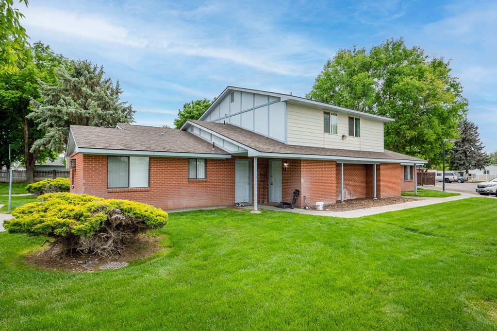 the front of a brick house with green grass and trees