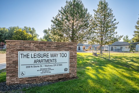 A sign for The Leisure Way Apartments stands in front of a grassy area.