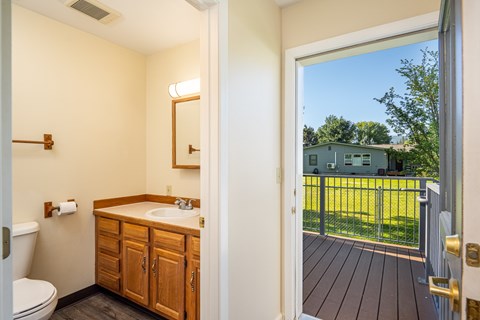 A bathroom with a wooden vanity and a view of a backyard through the door.