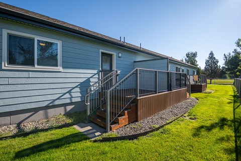 A house with a blue siding and a grey roof with a small porch and a metal railing.