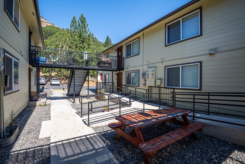 A sunny day at the outdoor patio of a building with a picnic table and stairs leading to a balcony.