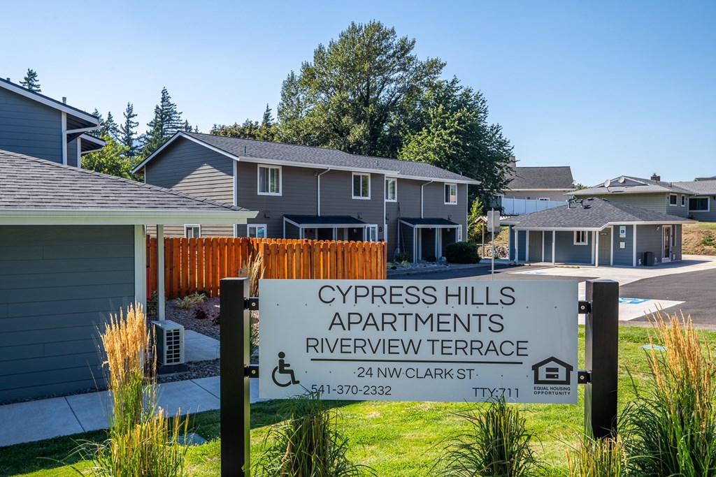 A sign for Cypress Hills Apartments stands in front of a building.