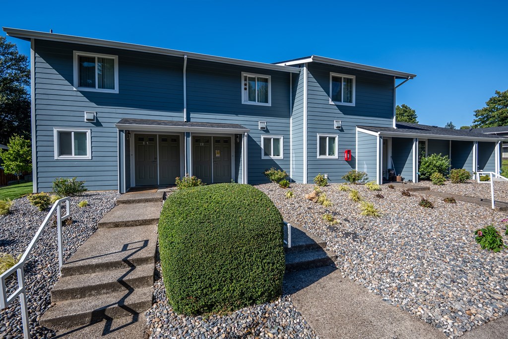 A grey house with a green bush in front.