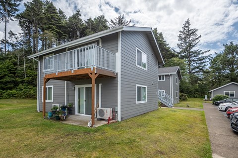 A grey house with a balcony and a green lawn.
