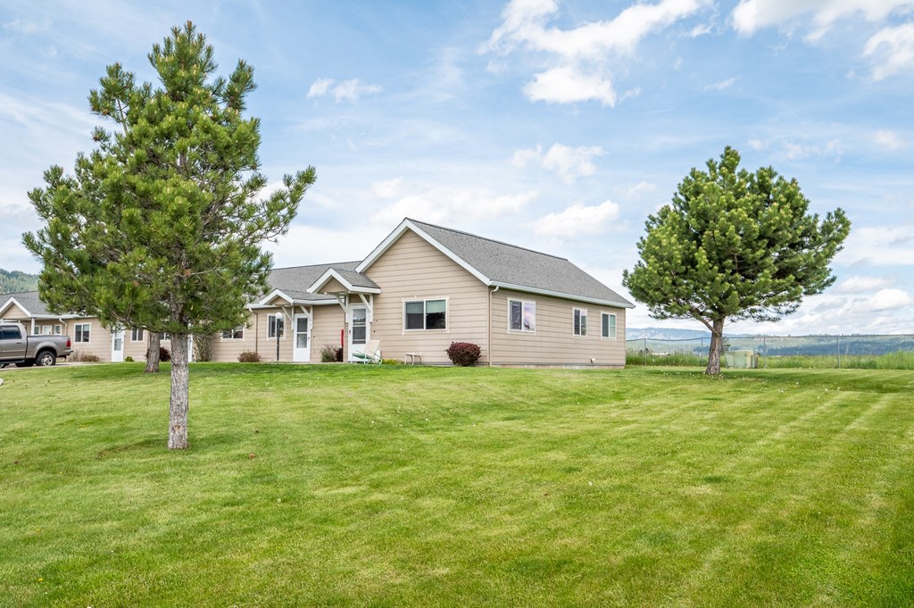 A house with a green lawn and two trees in front of it.