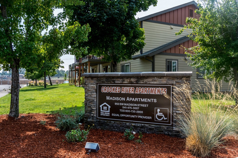 a sign in front of a building with a lawn and trees