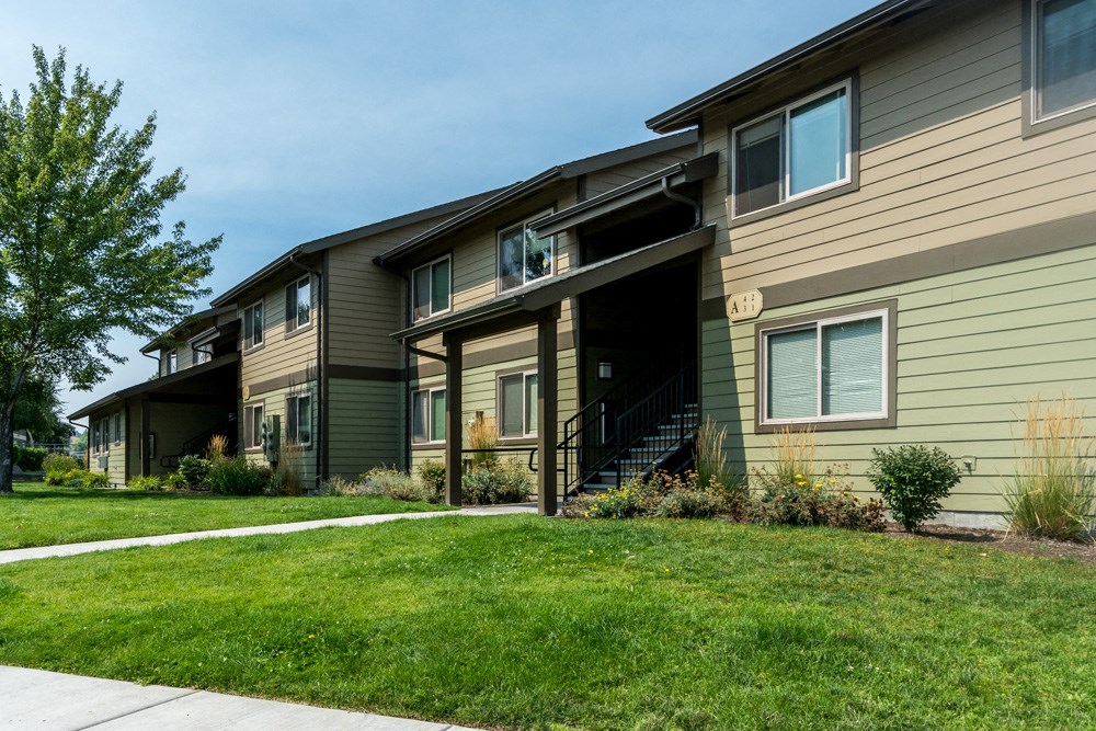 a green and brown house with a sidewalk in front of it