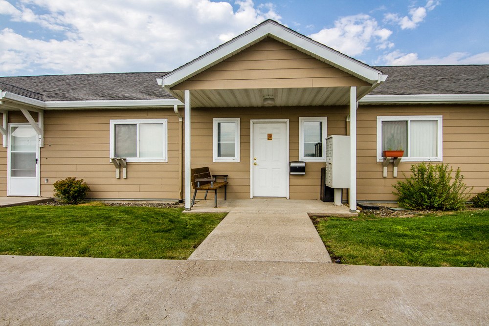 the front of a tan house with a white door and a sidewalk