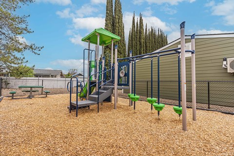 A playground with a green slide and a brown surface.