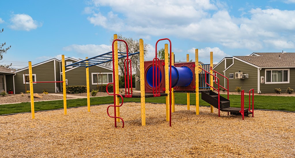 A playground with a red and blue slide, yellow poles, and a black ramp.