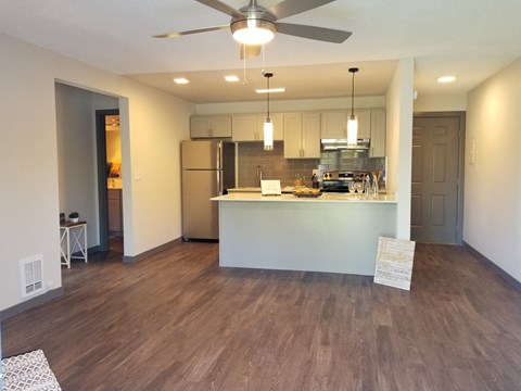 an empty living room with a kitchen and a ceiling fan