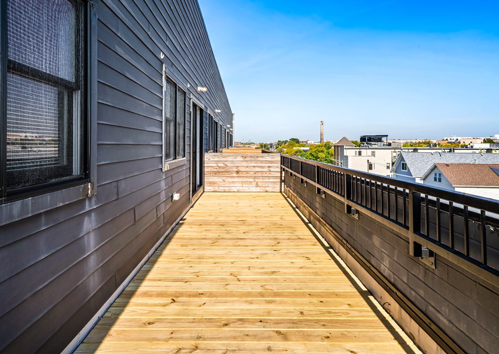 A wooden deck with a metal railing and a building with a grey siding to the left.