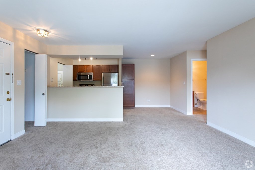 an empty living room with a kitchen with a microwave and a refrigerator