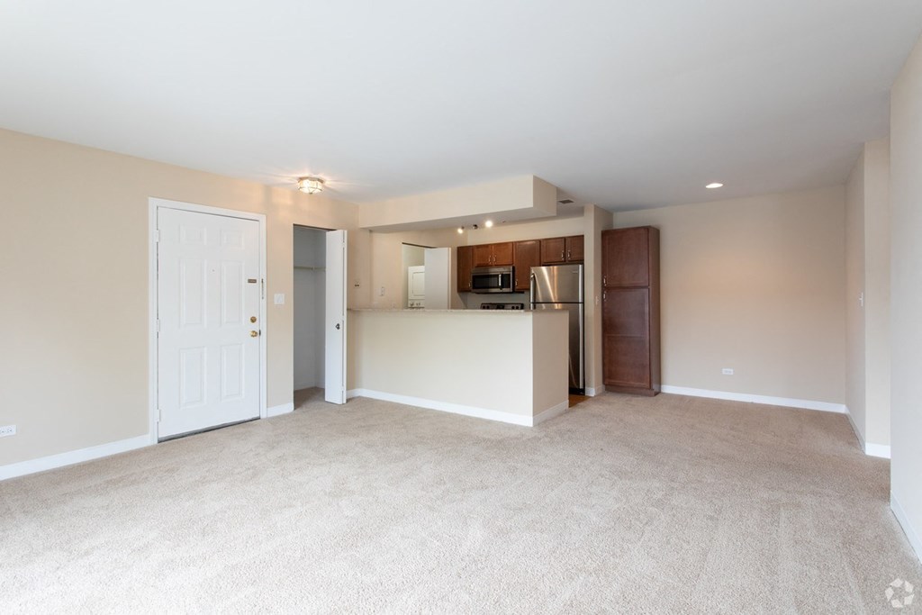 an empty living room with a kitchen in the corner