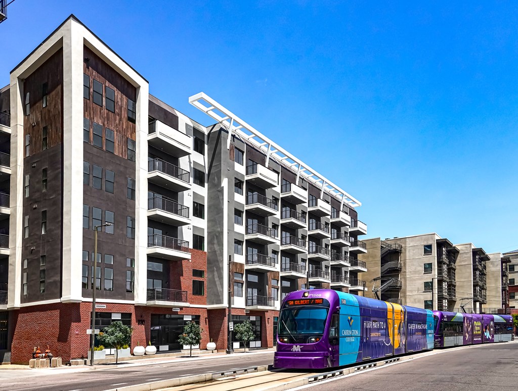 A purple train is on the tracks in front of a building.