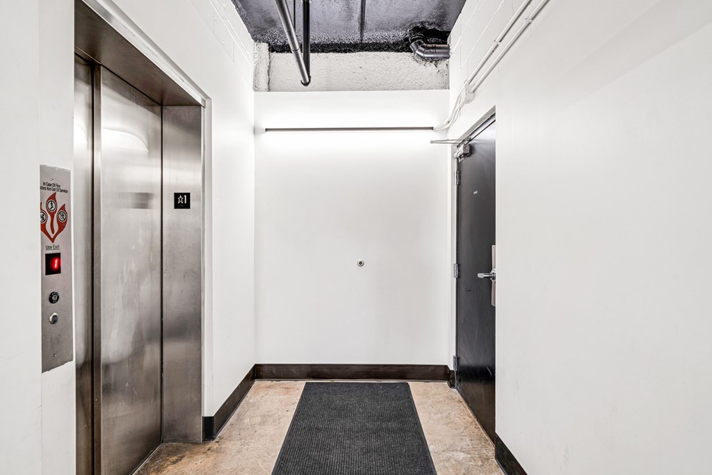 A hallway with a silver elevator on the left and a closed door on the right.