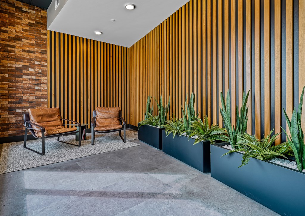 a lobby with two chairs and plants in front of a brick wall