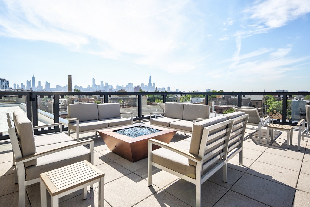 a roof deck with chairs and a fire pit and a city in the background