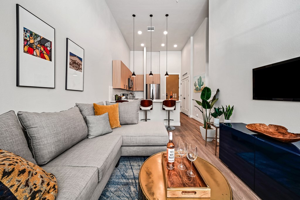A modern living room with a grey sofa, a wooden coffee table, and a TV on the wall.
