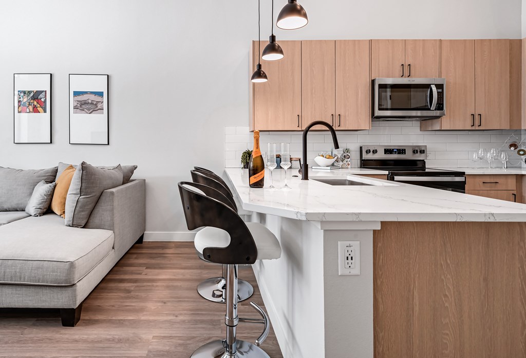 A modern kitchen with a white countertop and a grey couch with orange pillows.