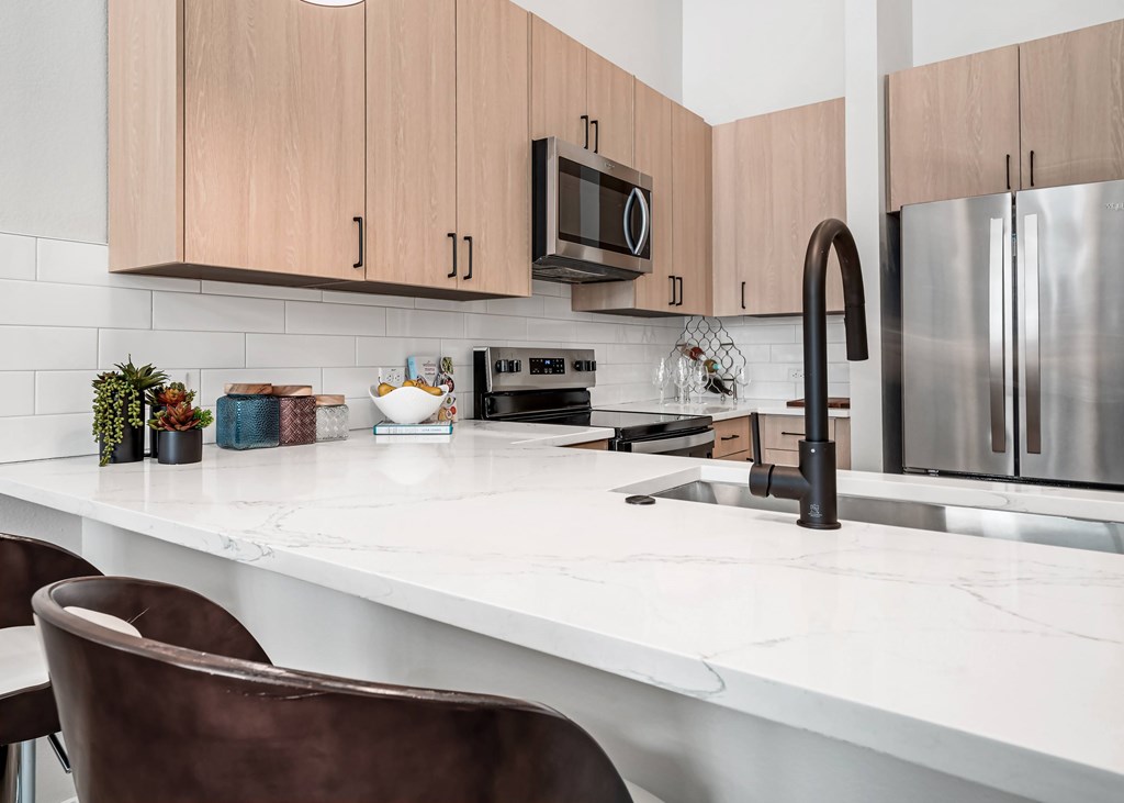 A kitchen with a white countertop and brown chairs.