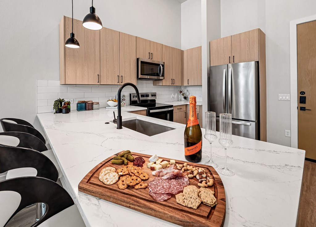 A kitchen with a cutting board of food and a bottle of wine on the counter.