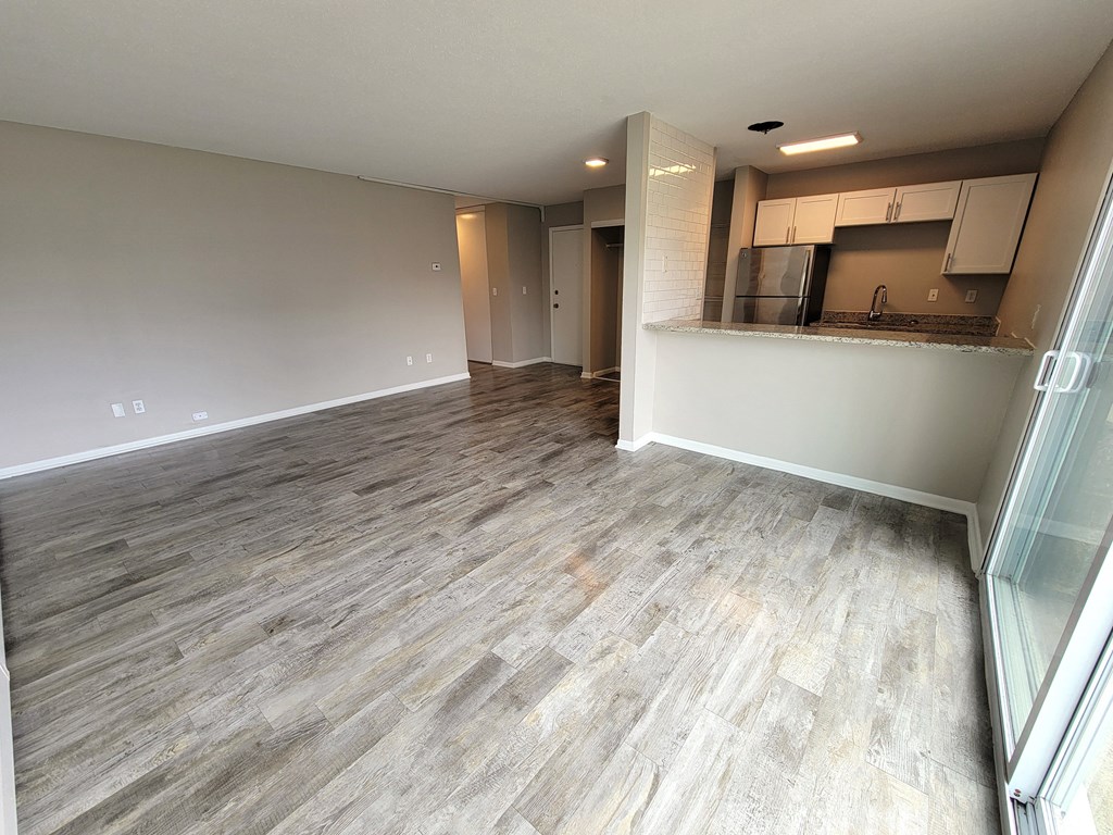 an empty living room with wood flooring and a kitchen