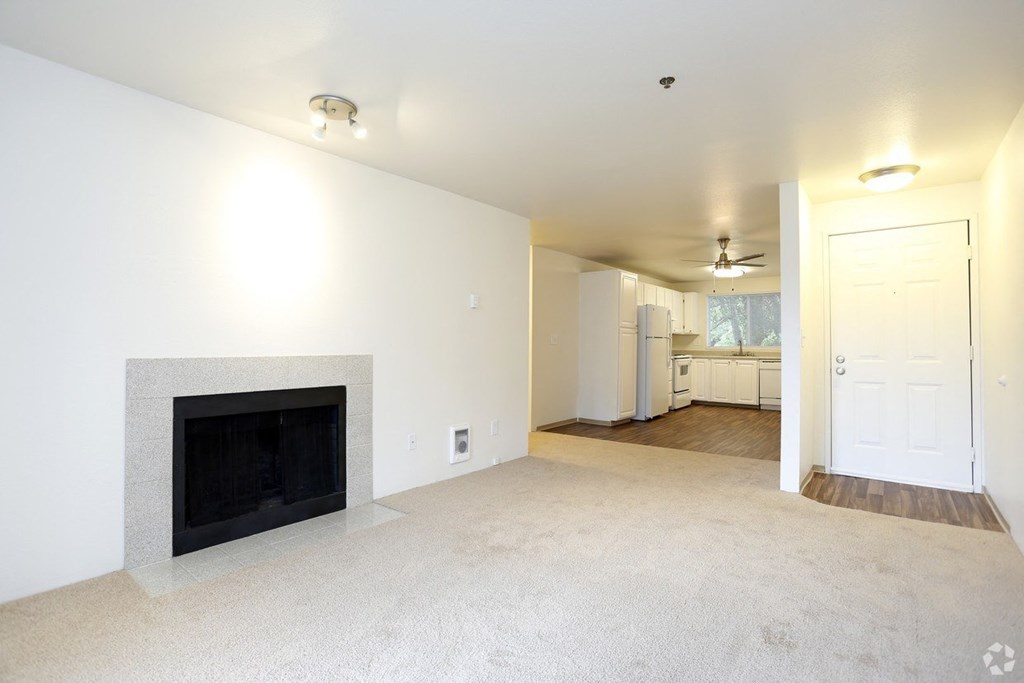 an empty living room with a fireplace and a kitchen
