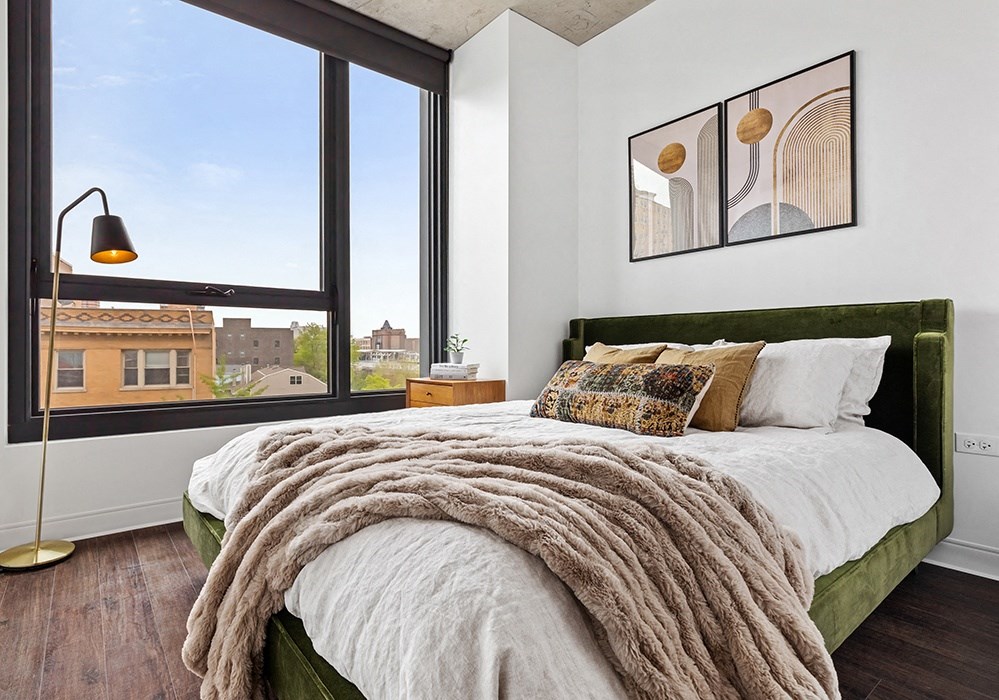 a bedroom with a large window and a bed with a blanket and pillows