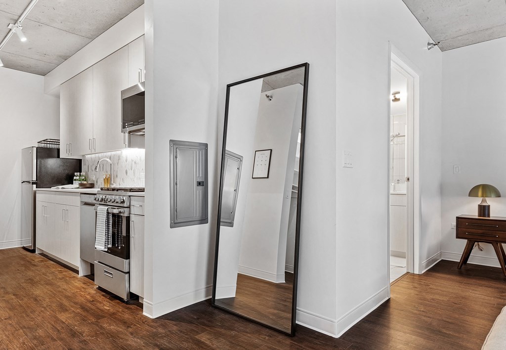 a living room with a mirror and a kitchen with a stove and refrigerator