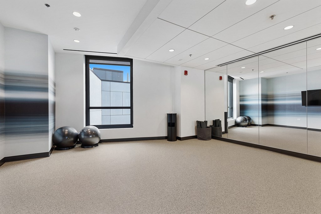 A spacious office room with a large window, a carpeted floor, and a glass wall.