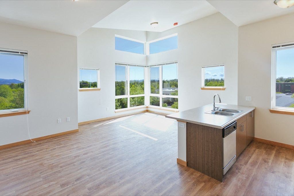 an empty living room with a kitchen and a large window