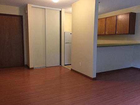 an empty living room with a wood floor and a refrigerator