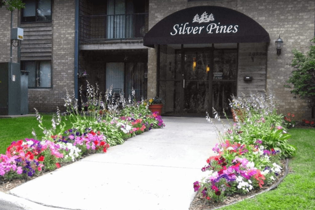 the sidewalk in front of the silver pines building with colorful flowers