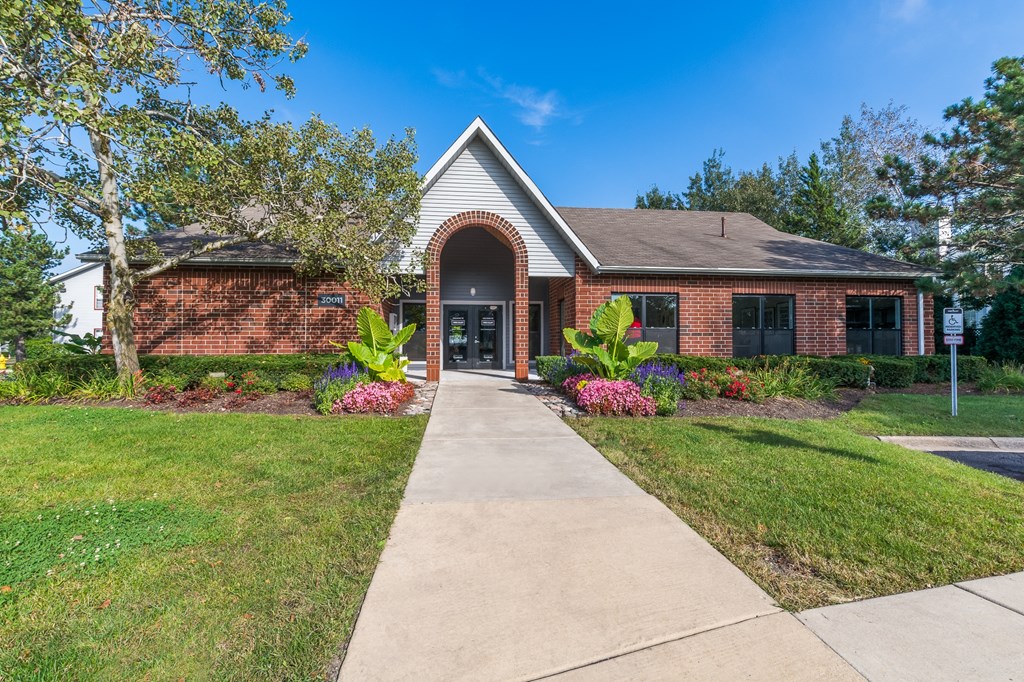 the front of a red brick building with a sidewalk and grass