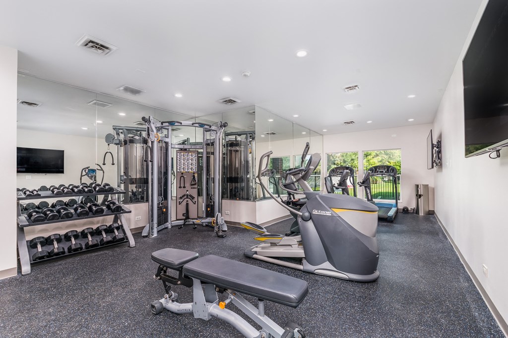 a gym with weights and cardio equipment and a tv on the wall