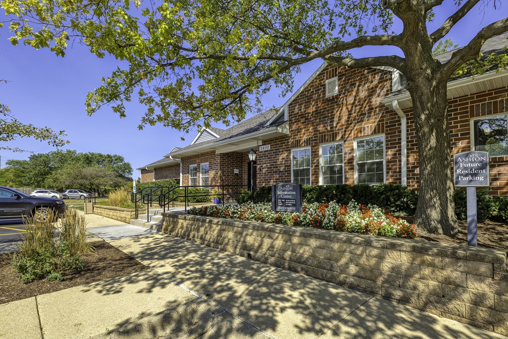 the front of a brick building with a tree and flowers in front of it