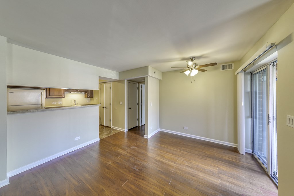 an empty living room with a kitchen and a ceiling fan