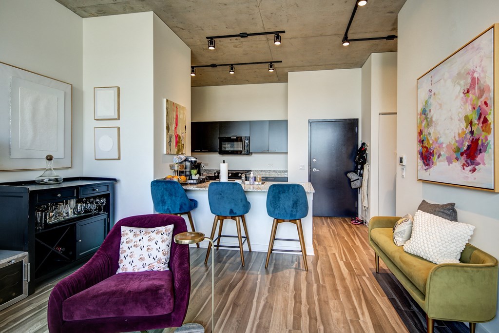 a living room with purple chairs and a kitchen with a bar and stools