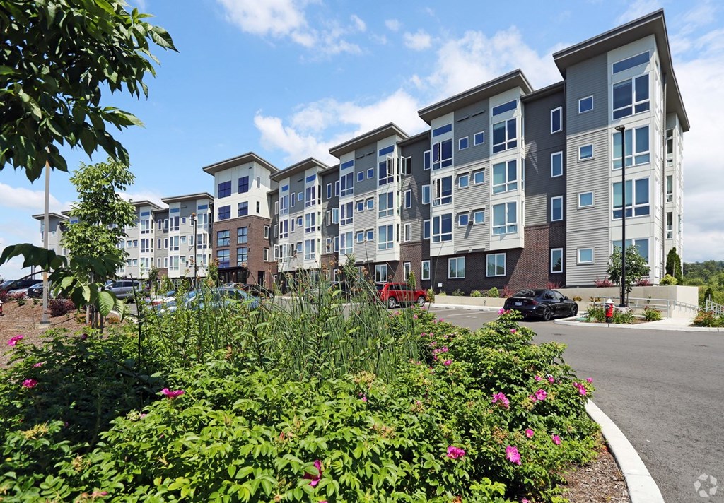 an exterior view of an apartment building on a street with flowers