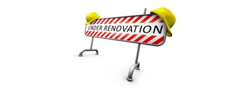 A sign that says "under renovation" is held up by two yellow construction helmets.