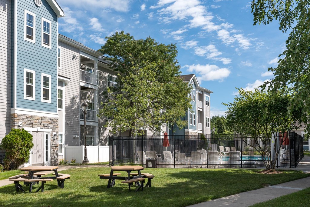 A sunny day at a park with picnic tables and apartment buildings in the background.