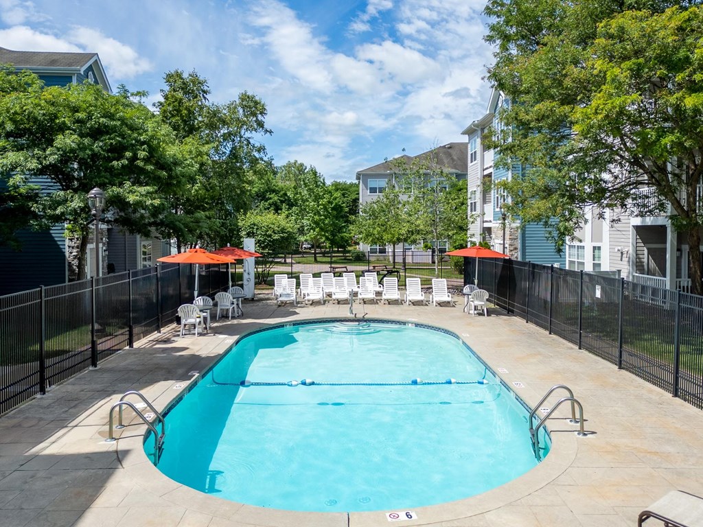 A swimming pool surrounded by a black fence and trees at The Commons at Drum Hill
