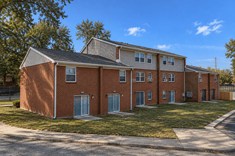 A red brick apartment building with a green lawn in front.