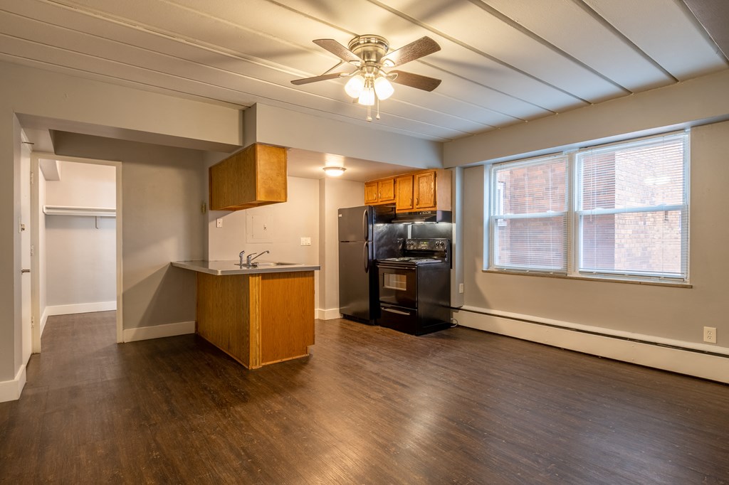 an empty living room with a ceiling fan and a kitchen