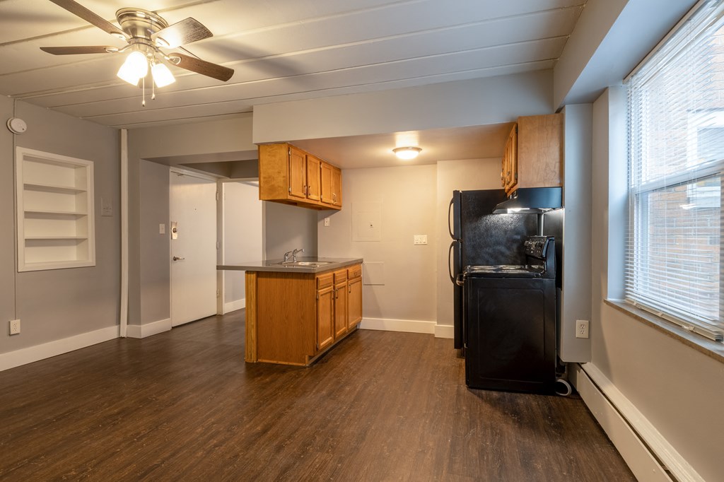 an empty living room with a kitchen with a black refrigerator
