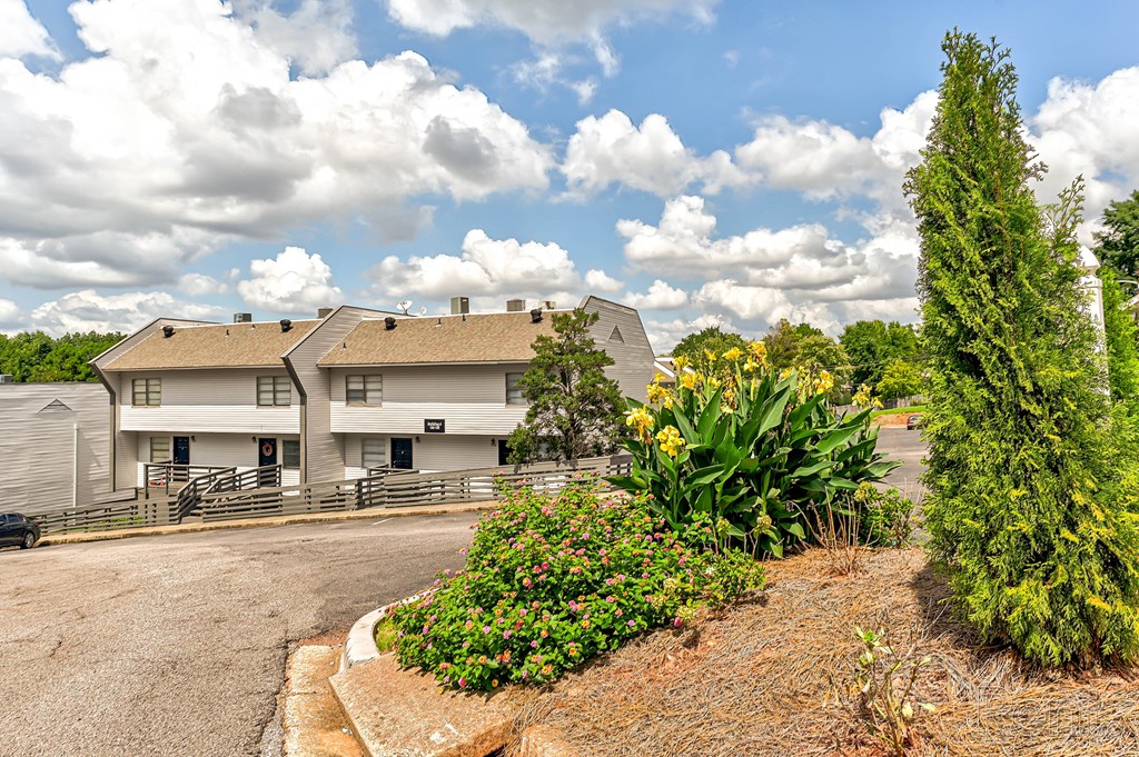 A white building with a grey roof is surrounded by a garden with a variety of plants and flowers.