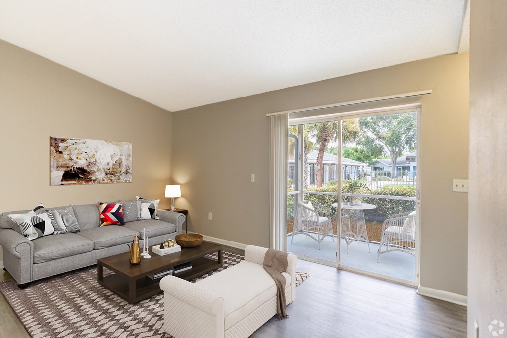 a living room with a couch and a chair and a sliding glass door at Aqua Bay Apartments in Naples, FL 34116