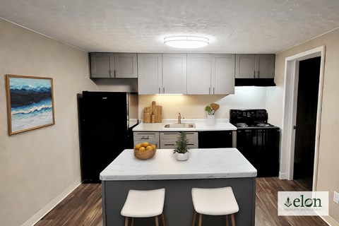 A kitchen with a black refrigerator, white cabinets, and a painting on the wall.