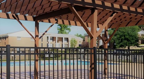 A pool area with a black fence and a brown pergola.